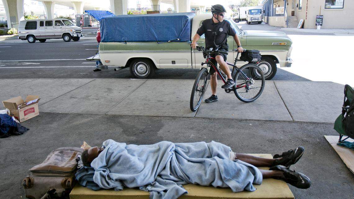 A Boise police officer stops his bike in front of homeless residents under the South 16th Street bridge in September 2014.