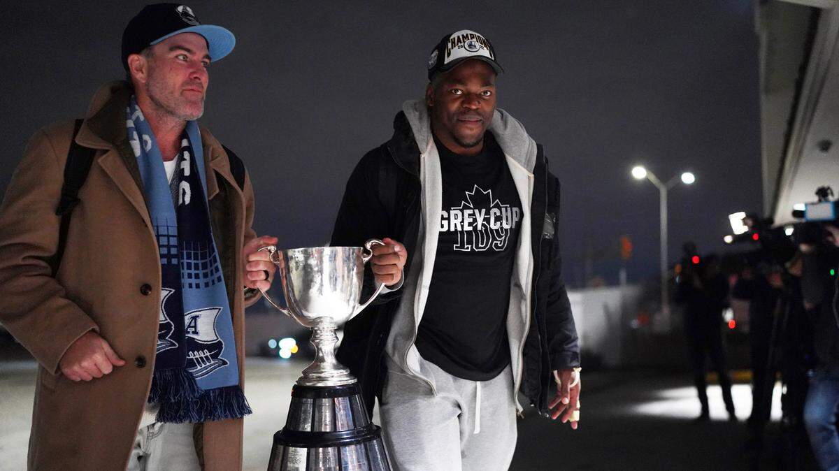 Toronto Argonauts head coach Ryan Dinwiddie and linebacker Henoc Muamba carry the Grey Cup trophy into Toronto Pearson International Airport. The Argonauts defeated the Winnipeg Blue Bombers on Sunday to win the cup.