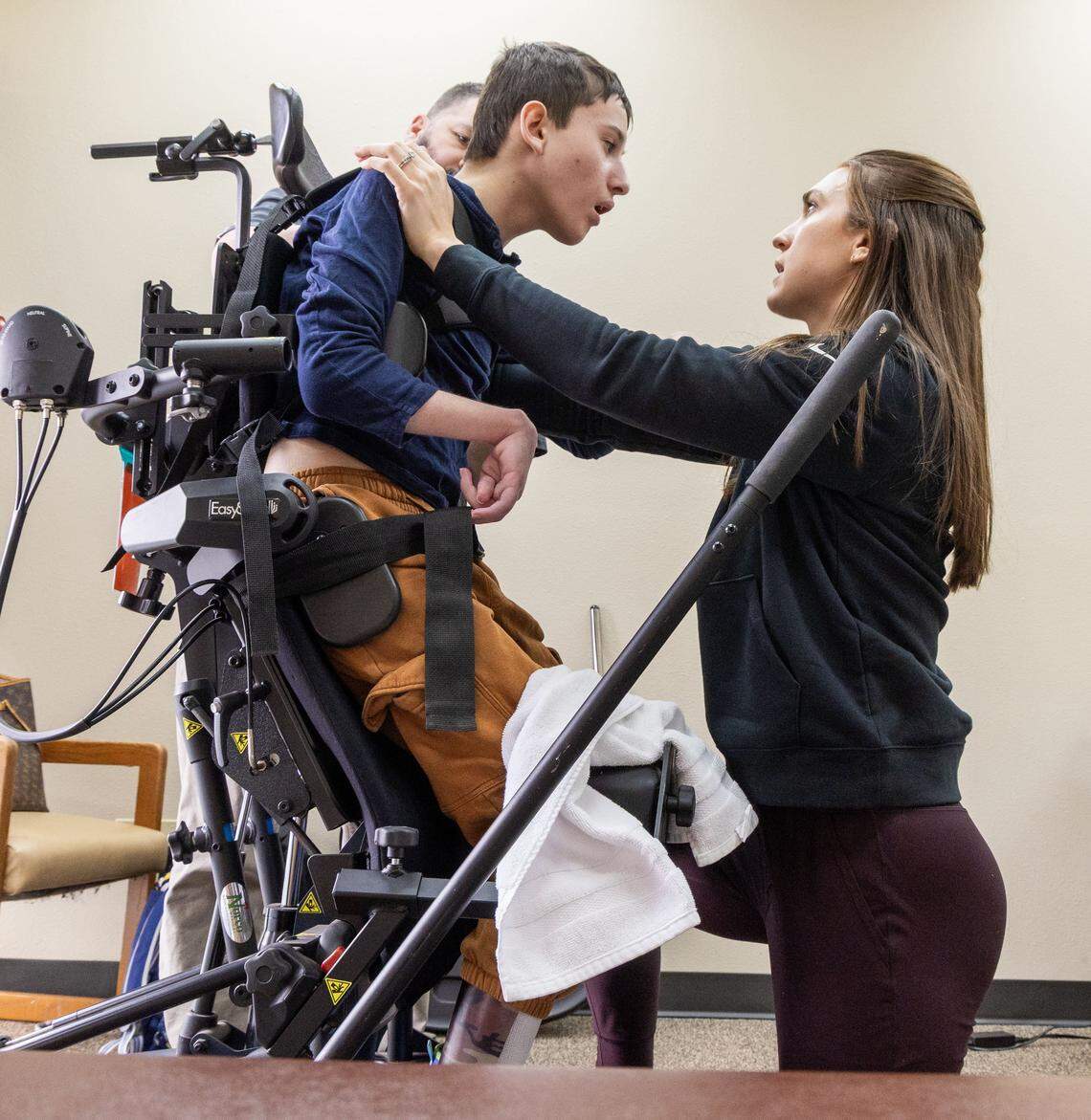 Physical therapist Bri Clover works with Evan Kates, 11, in his new “standing chair” at Kaleidoscope Pediatric Therapy in Boise. The vertical platform, being fitted by Norco's Jeremy Monaghan, will assist Evan to a standing position to help build strength and stamina.
