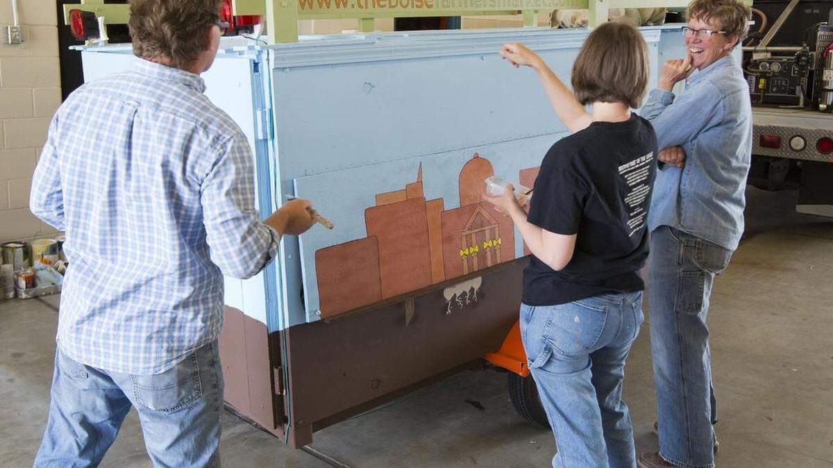 Janie Burns, right, marvels at how her simple trailer has transformed into a rolling art piece with Birgit Phelps, center, and Earl Swope. A group of art students gathered to help paint Burns’ mobile farmer’s market at Fire Station No. 2 in Boise where Swope also is stationed as a firefighter.