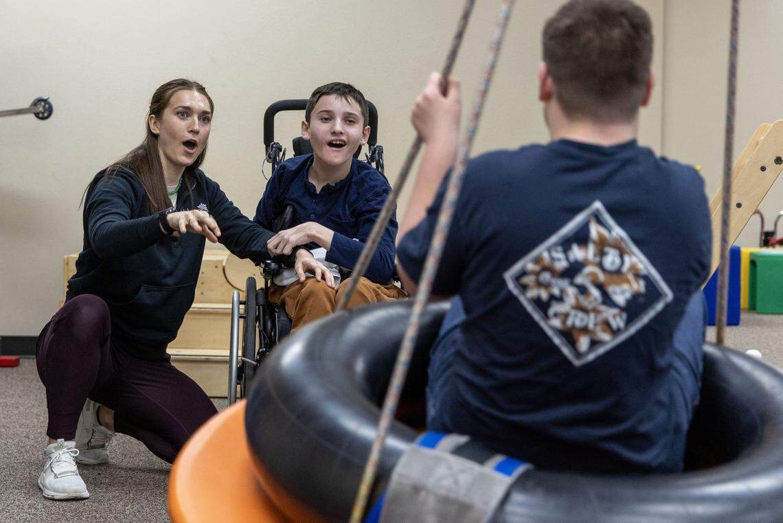 Confined to wheelchair, Evan Kates, 11, has some fun with Jacob Holden, 15, a fellow client at Kaleidoscope Pediatric Therapy in Boise. Evan's therapist Bri Clover helps him improve motor skills as they toss fake snowballs at Jacob swinging on a pendulum.