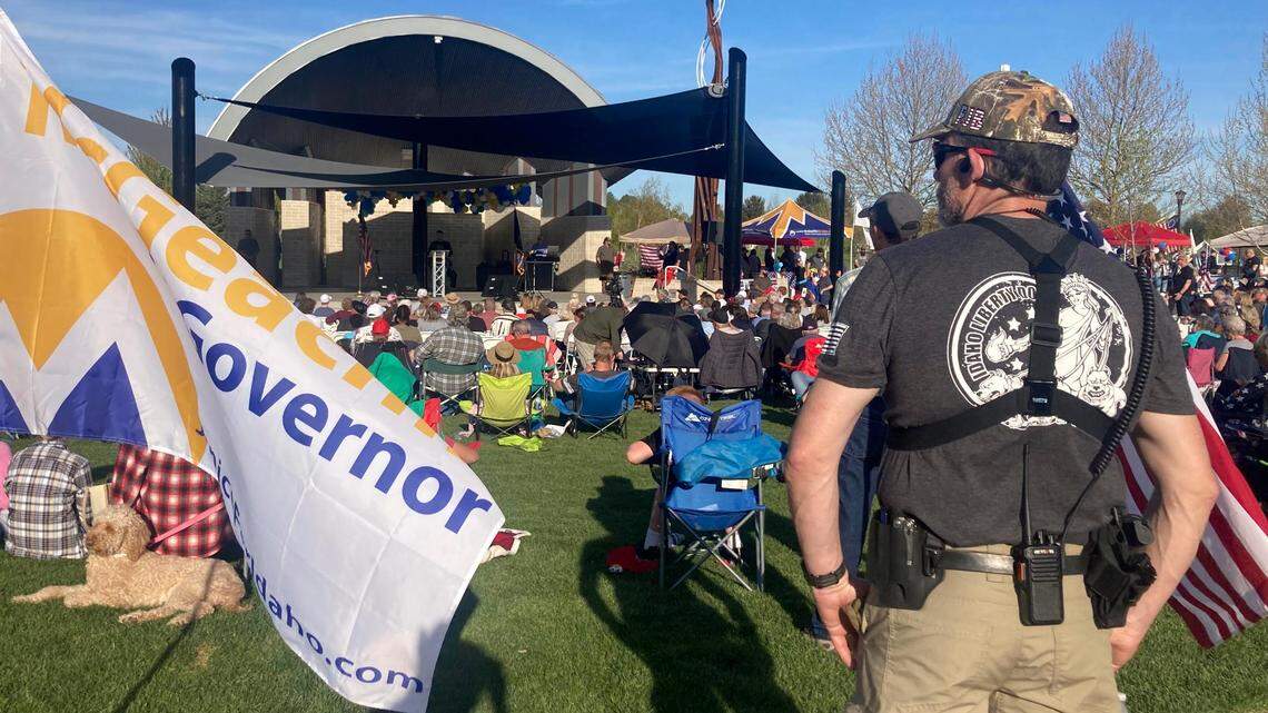 A member of the Idaho Liberty Dogs, a right-wing citizen group, stands guard with a holstered handgun, walkie-talkie and earpiece at a campaign rally in 2022, at Julius M. Kleiner Memorial Park in Meridian.