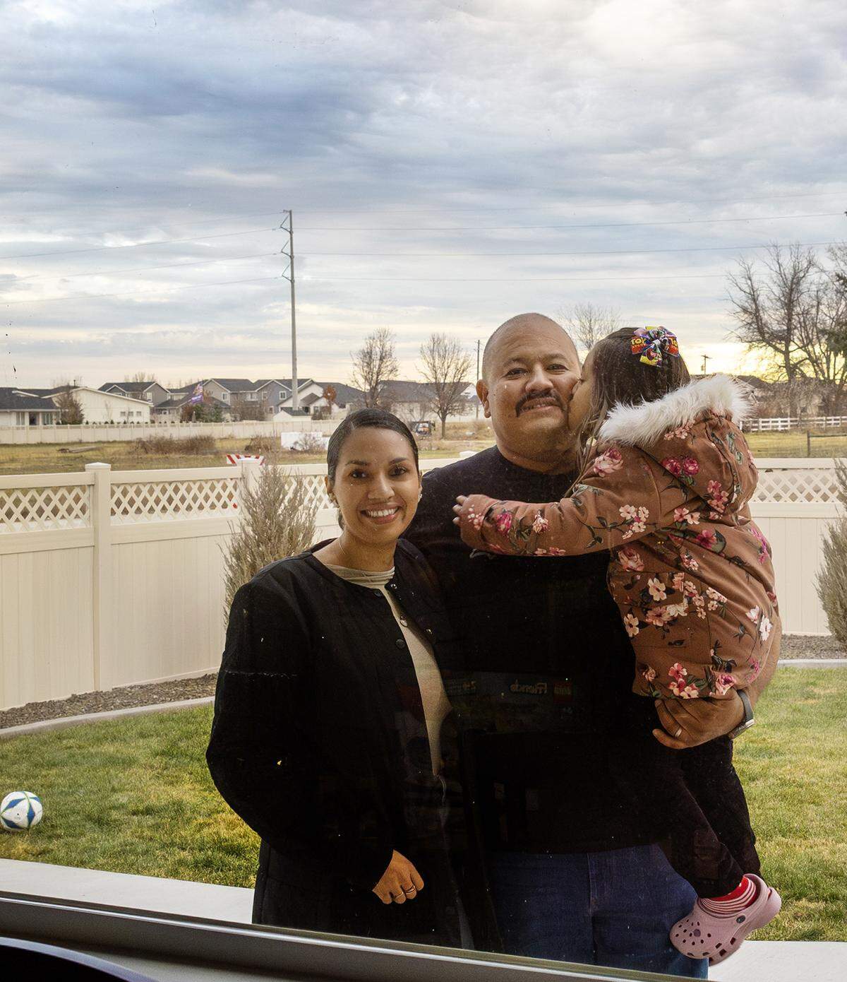 Jorge Grajeda, with his wife, Marllin, and daughter, Samantha, 4, framed through the living room window of their rural home near Eagle.