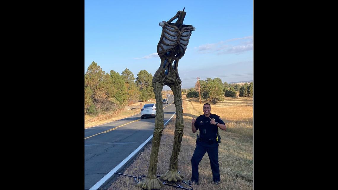 A deputy poses next to a headless 12-foot prop skeleton found early Saturday morning on a Colroado roadway.
