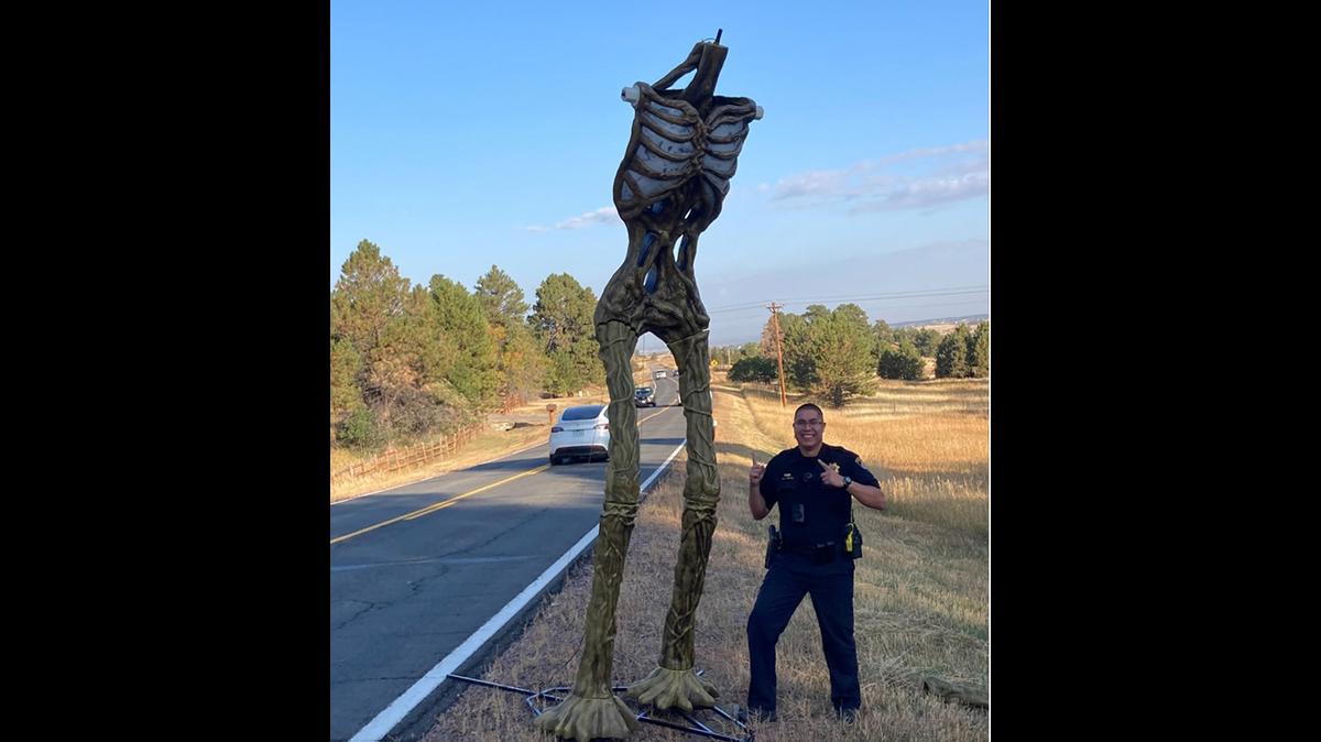 A deputy poses next to a headless 12-foot prop skeleton found early Saturday morning on a Colroado roadway.