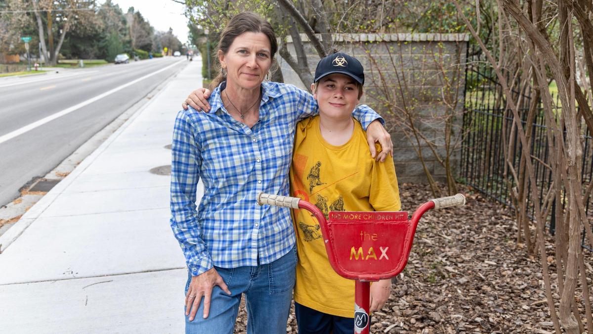 Courtney Madigan and her son Max Wyatt, 14, stand on the sidewalk next to a marker where Max was hit by a car while riding a bicycle in 2015 on on Kootenai Street.