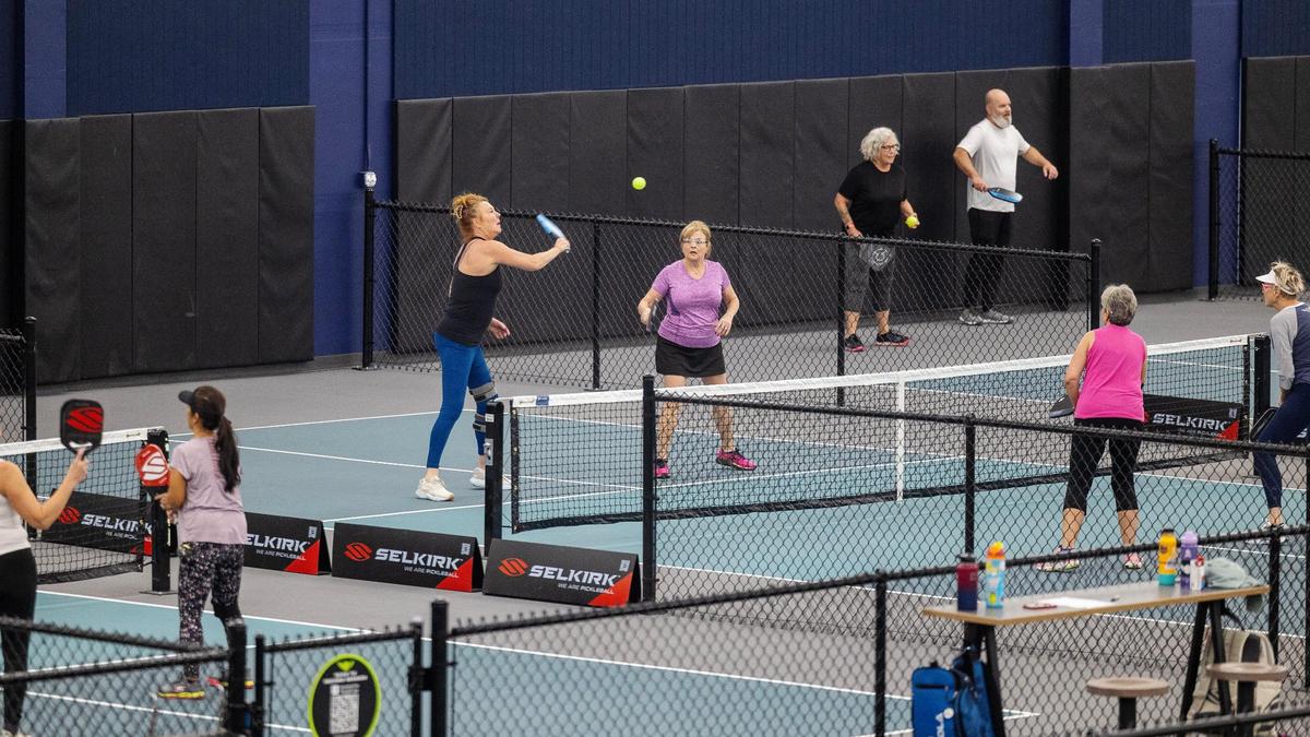 People play indoor pickleball at The Flying Pickle. The sport resembles tennis but uses a smaller court, paddles more akin to large ping-pong paddles, and a large, whiffle-ball-like ball.