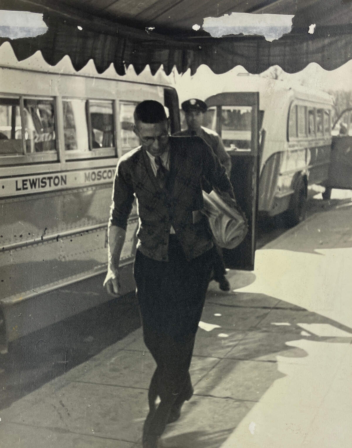 Orville Jackson walks along the sidewalk outside of his drug store, a bundle of newspapers tucked under his arm, sometime between 1950 and 1965.