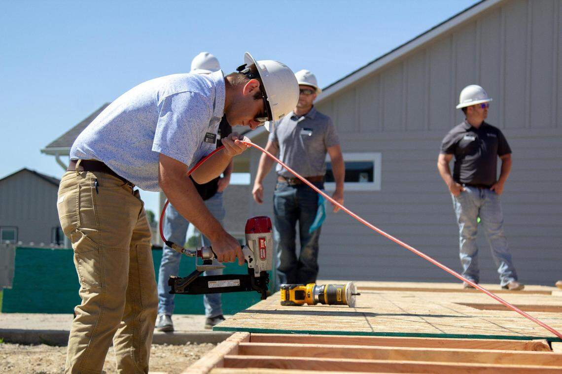 Darren Henry, of Hayden Homes, uses a nail gun to secure the plywood to the frame of the house on June 14, 2023.