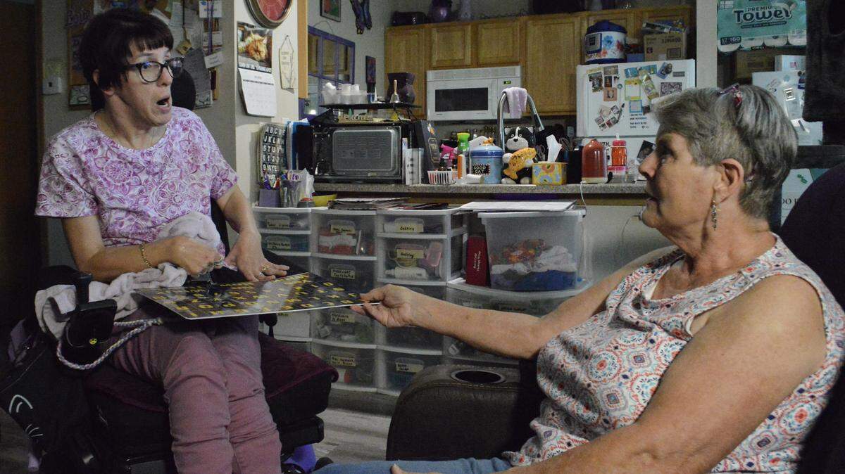 Kristyn Herbert, left, uses a board with the alphabet and numbers with the assistance of her in-home caregiver and friend Mary Arndt to communicate.