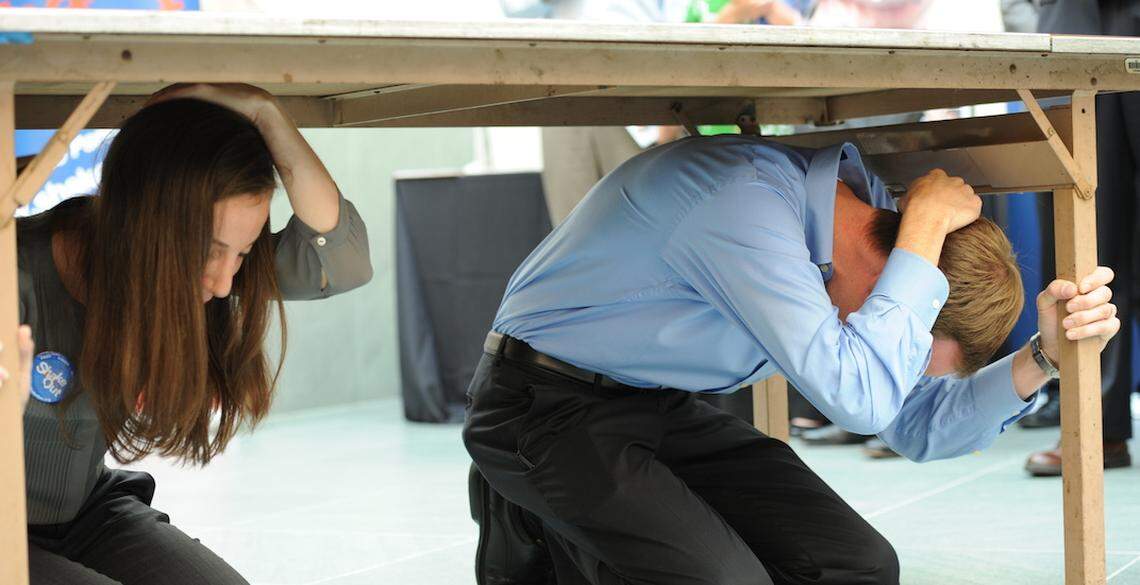 Two people bending over underneath a desk