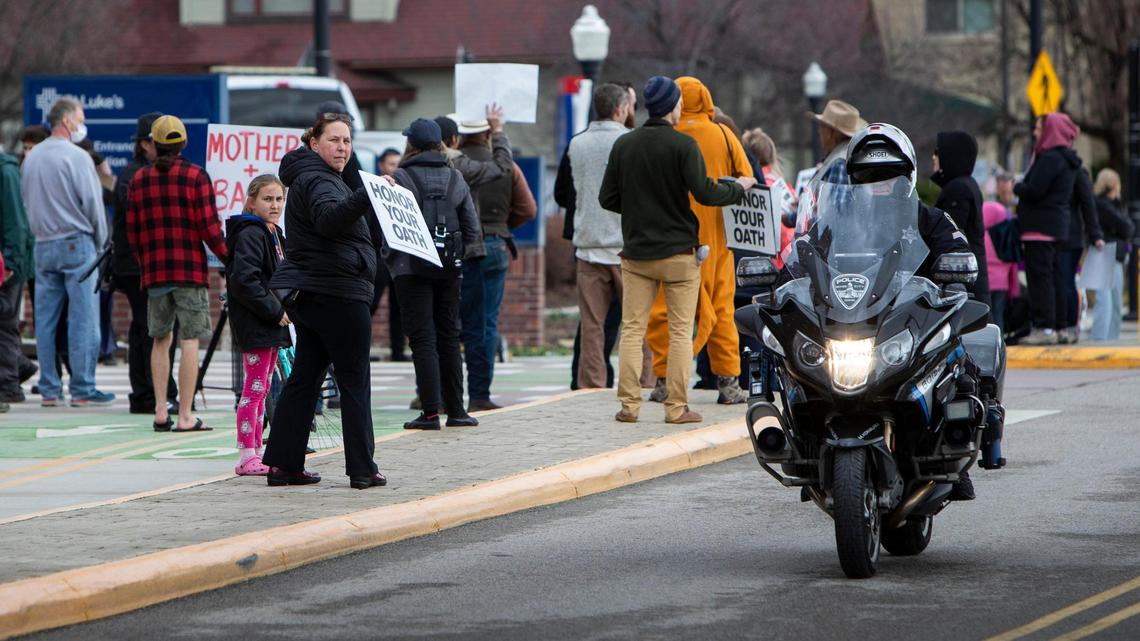 A protester holding a sign directed to police, shouts “baby snatchers” at a Boise police officer patrolling the area outside of St. Luke’s Boise Medical Center. Protesters swarmed the medical complex Tuesday, March 15, 2022, causing security to lock down the complex.
