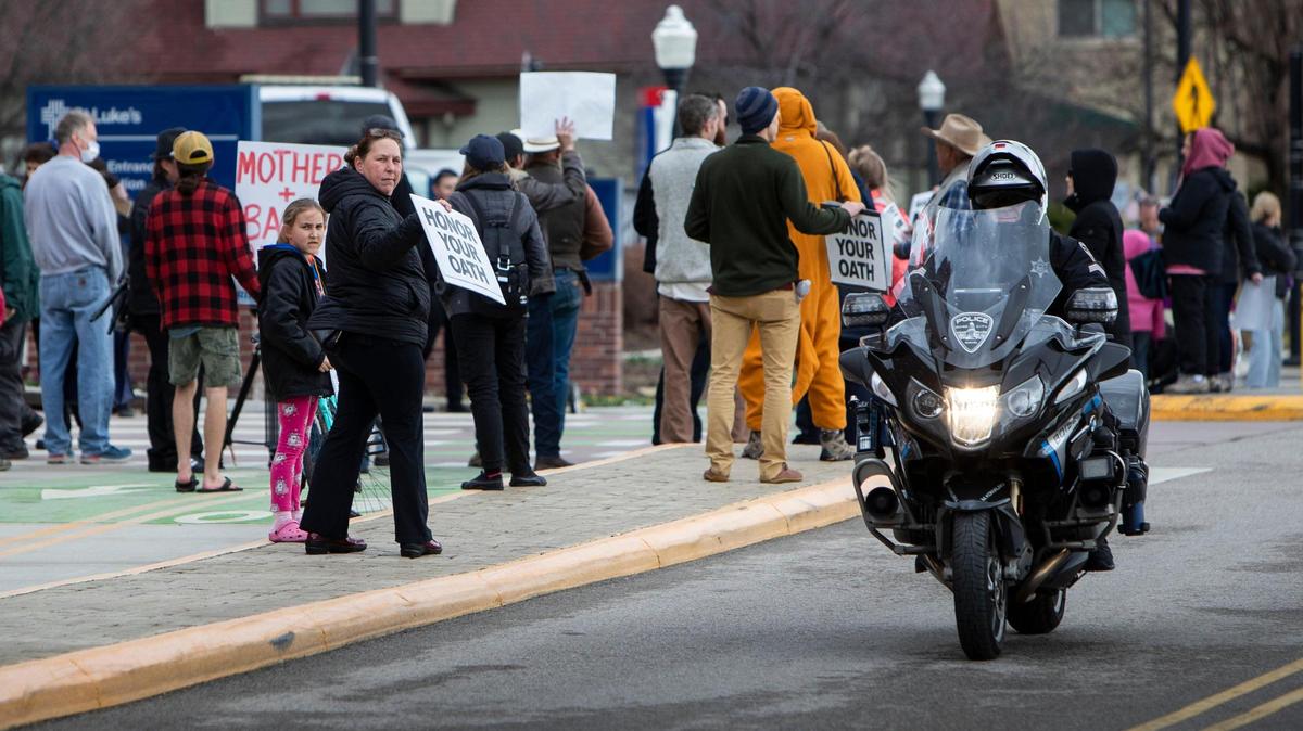 A protester holding a sign directed to police, shouts “baby snatchers” at a Boise police officer patrolling the area outside of St. Luke’s Boise Medical Center. Protesters swarmed the medical complex Tuesday, March 15, 2022, causing security to lock down the complex.