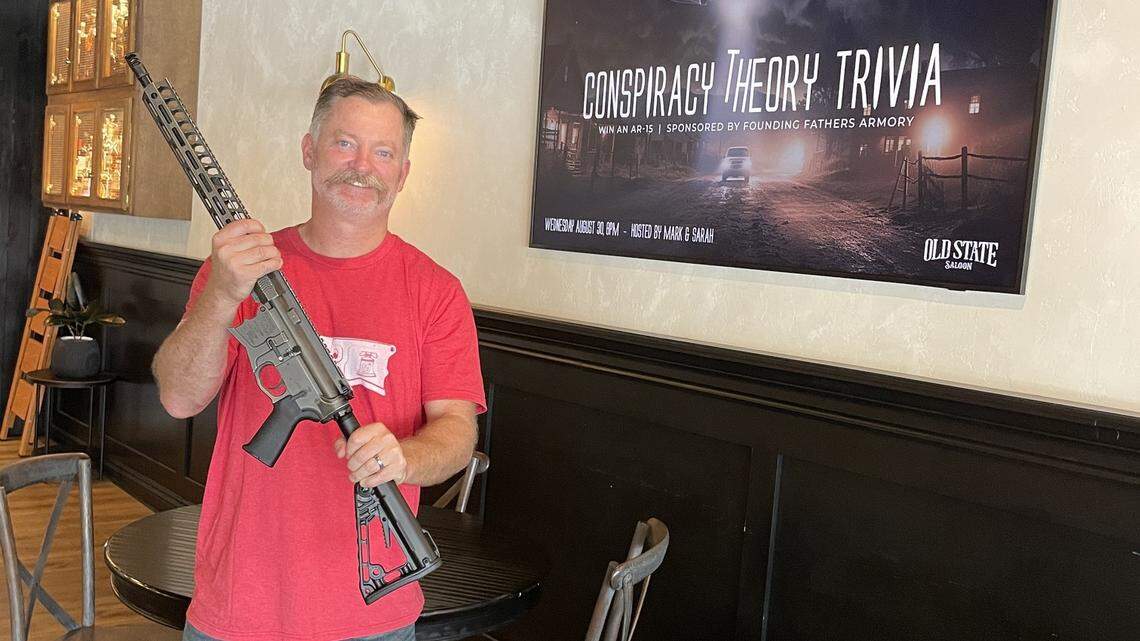 Old State Saloon owner Mark Fitzpatrick holds the AR-15 rifle that will be used as a prize.