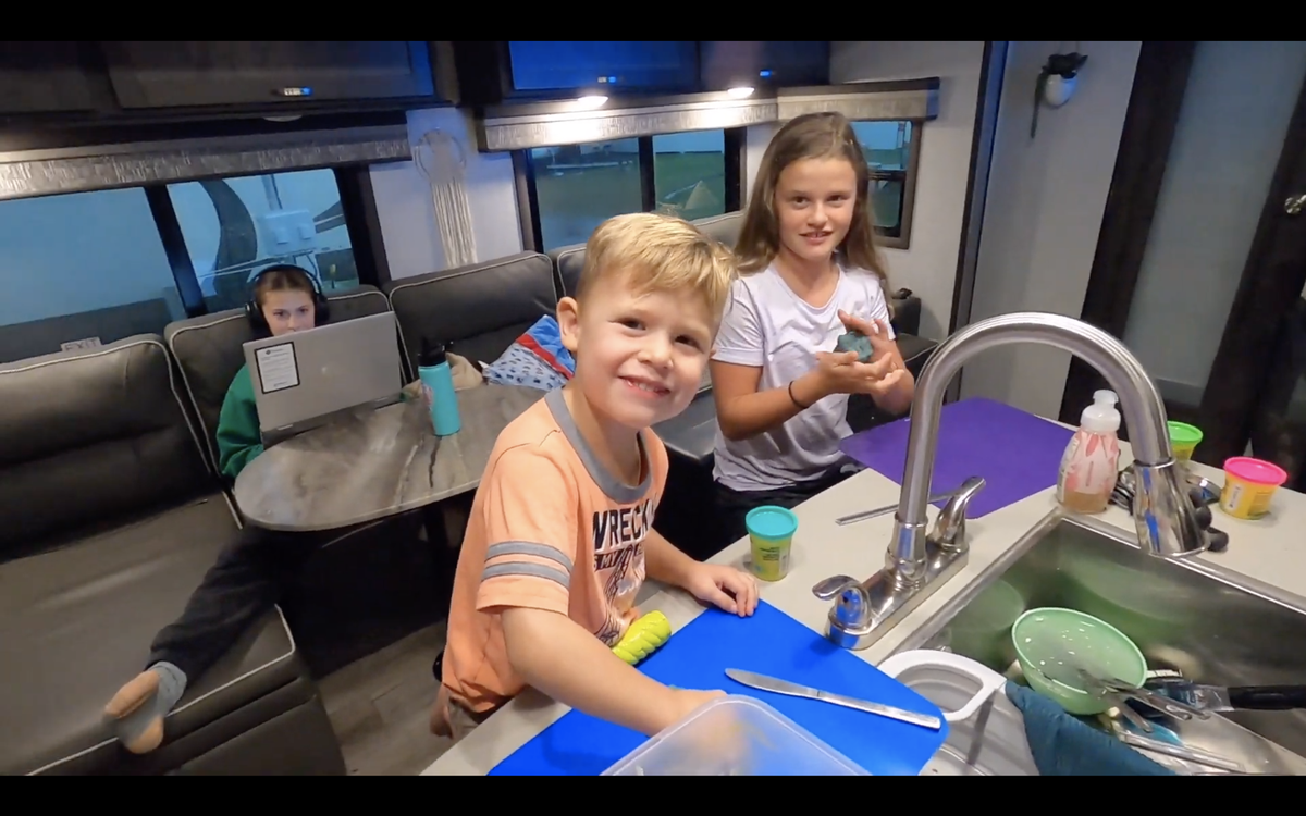 Three-year-old Koen and 10-year-old Brittan play at the RV kitchen island while 15-year-old Jadyn works on online schooling in the background.