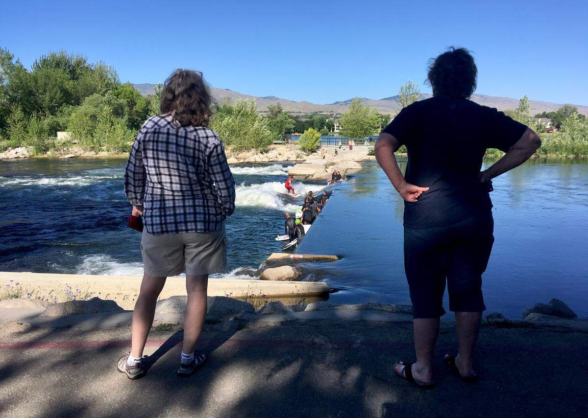 Two women watch as surfers take on the waves at Whitewater Park. Many of the surfers park along 34th Street and change in the back of their trucks. Developer Hannah Ball wants to build showers and changing areas for them nearby.