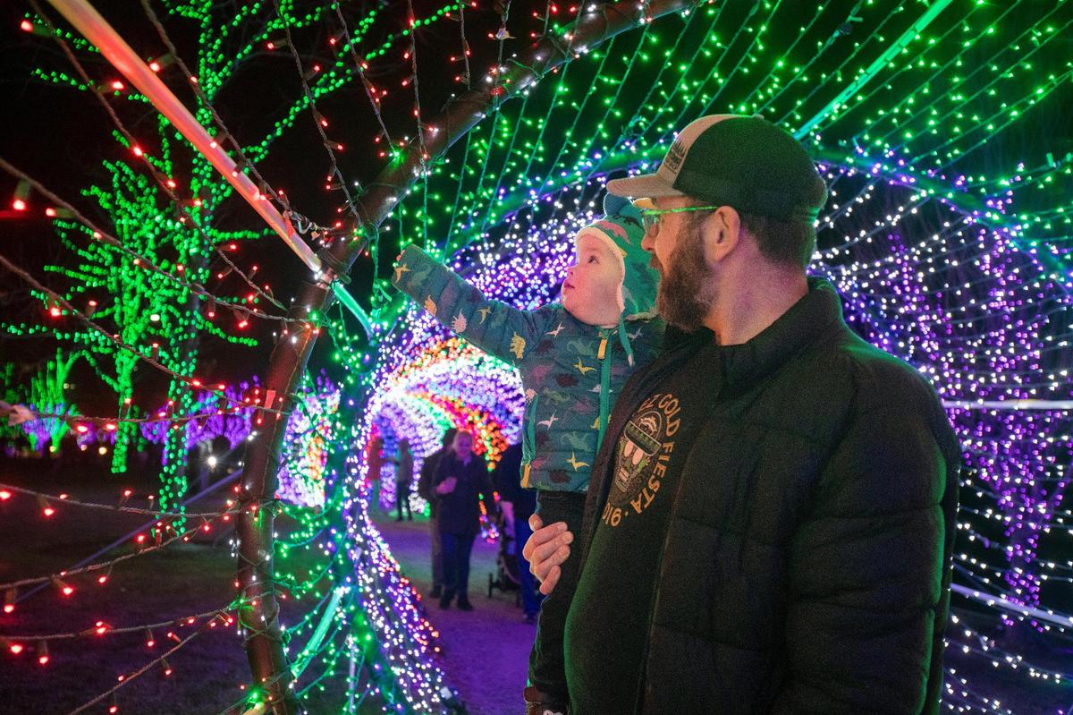 Danny Merrill of Boise holds his son Walter Merrill, 1, as they walk through a tunnel of Christmas lights at Scentsy Commons in Meridian on Tuesday, Dec. 21, 2021. The free display of over 800,000 lights runs through Jan 16.
