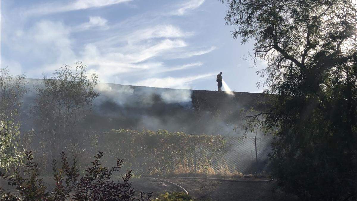 A firefighter stands on a road along the New York Canal and sprays water on a brush fire that burned along the hillside Friday, Sept. 14, 2018.