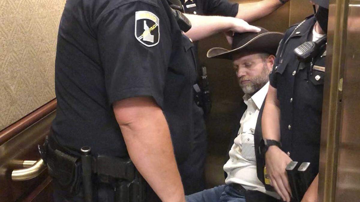 This image taken from video shows anti-government activist Ammon Bundy, rear, being wheeled into an elevator in a chair following his arrest at the Idaho Statehouse in Boise, Idaho, Tuesday, Aug. 25, 2020. Authorities arrested Bundy after he refused to leave a meeting room where a few hours earlier angry protesters forced out lawmakers. (AP Photo/Keith Ridler)