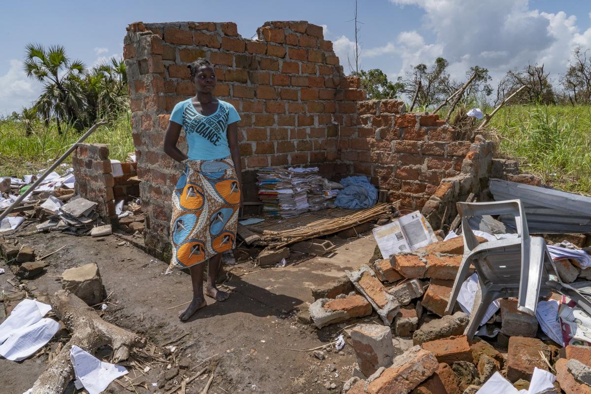 Professora Ana Jo, a first-grade teacher, stands next to the remains of her school and piles of books that she has set aside to dry and save. Teams from Gorongosa brought food to this neighborhood in the aftermath of Cyclone Idai near Gorongosa National Park. The park has pledged to help rebuild the school.