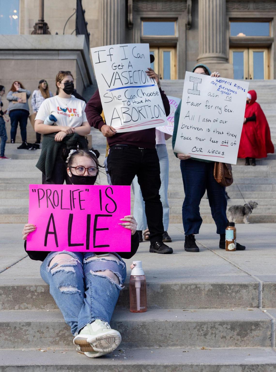 Kaitlyn Kirk of Boise, foreground, sits with a sign while Bosians Robert Olson and Amanda Sammartano stand in the background with signs in in front of the Idaho State Capitol Building on Tuesday in response to the news of the Supreme Court draft leak indicating that Roe v. Wade and Planned Parenthood v. Casey will be overturned.