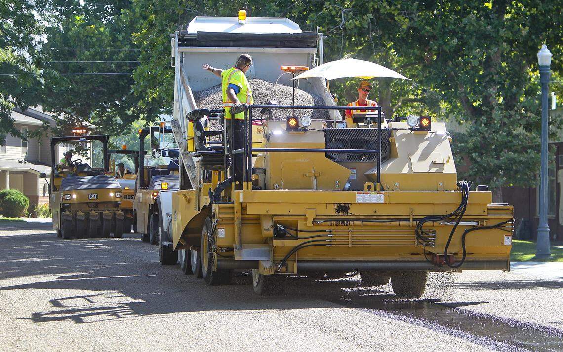 Ada County Highway Department workers on a chip-spreader vehicle distribute gravel over a polymer-infused oil while performing chip-seal work on South 12th Street in Boise in 2015. Several rubber-tire roller vehicles follow the chip spreader and push the gravel into the oil.