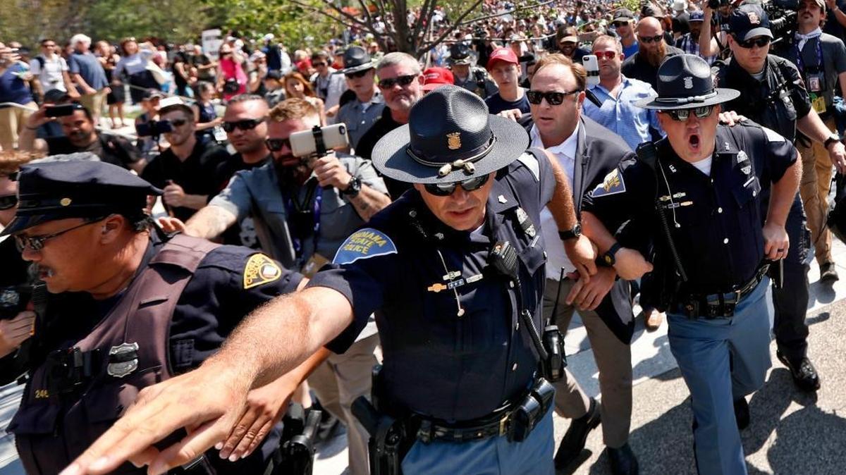 Alex Jones, second from right, is escorted by police from a crowd of protesters last July after he said he was attacked in Public Square in Cleveland during the second day of the Republican National Convention.