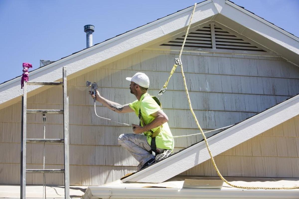 Although being tethered to a harness is a hassle because of the frequent adjustments, each adjustment makes workers aware, said Risa Roe, who oversees safety at Adam Roe Painting. “You have to be thinking safety all the time,” Roe said. Foreman Ryan Belieu paints the second story of a home, safely anchored to a cleat on the roof.