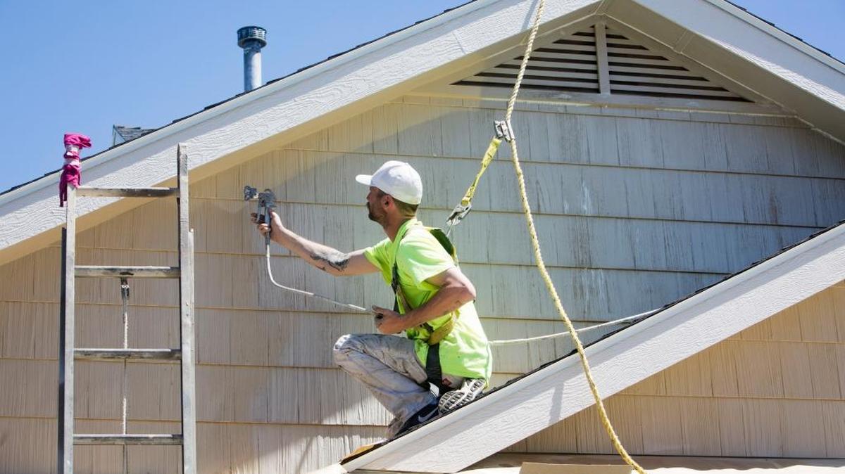 Ryan Belieu paints the second story of a home, safely anchored to a roof. Belieu’s employer — Adam Roe Painting, or ARP — has a strong focus on worker safety.