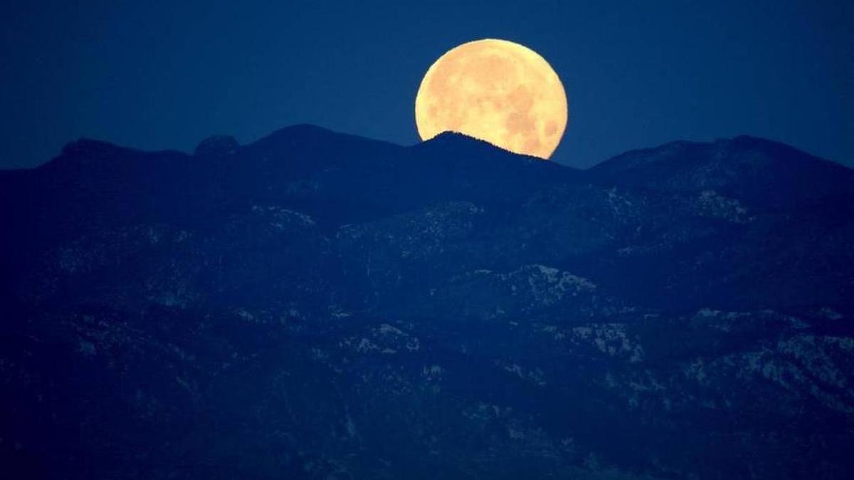 A full moon sets beyond the Rocky Mountains beyond Denver.
