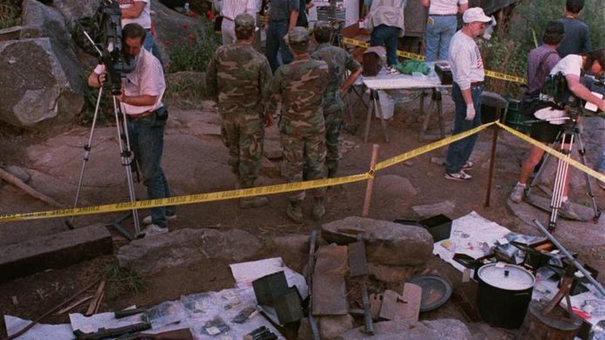 In this archive photo, federal agents and members of the media tour the outside of Randy Weaver’s home on Sept. 1, 1992. Confiscated guns and ammunition are displayed on the ground following the end of the 11-day standoff.
