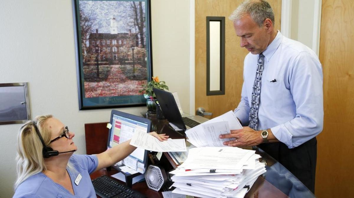 Dr. Richard Radnovich (right) and administrative assistant Lindsay Beacham, both with Injury Care Medical Center in Boise, talk next to patient history files waiting to be sent to pharmacy benefit insurance companies. Radnovich says health insurers are sometimes telling him to prescribe morphine and fentanyl before less-addictive drugs like Butrans.