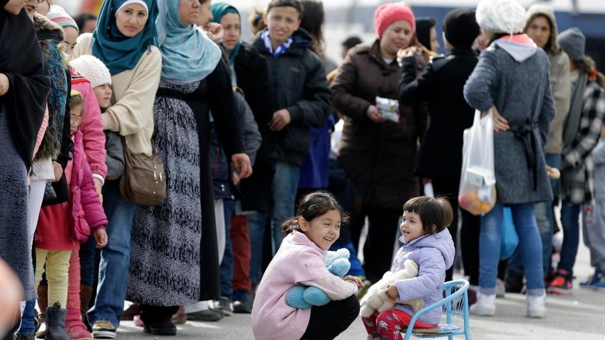 Children play as people wait Monday, March 7 in a queue to receive food distributed by non-governmental organizations at Athens' port of Piraeus, where over 2,000 stranded refugees and migrants stay at the passenger terminal buildings and their tents. European Union leaders will be looking to boost aid to Greece as the Balkan migrant route is effectively sealed, using Monday's summit as an attempt to restore unity among the 28 member nations after months of increasing bickering and go-it-alone policies.