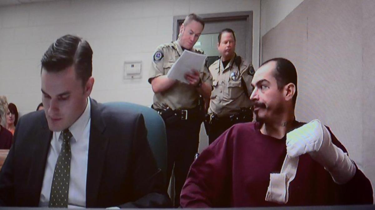 Patrick A. Zavala shows his injured hand during a video arraignment hearing in November. Public defender Abraham Wingrove, left, represents Zavala in the case.