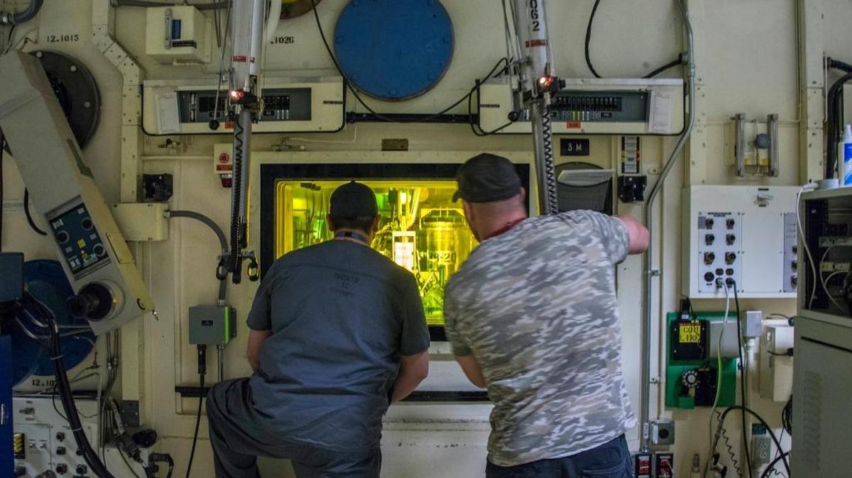 Freddy Rodriguez, left, and Brian Simmons, process nuclear operators at the INL, use master-slave manipulators to work with radioactive material on the other side of the glass.