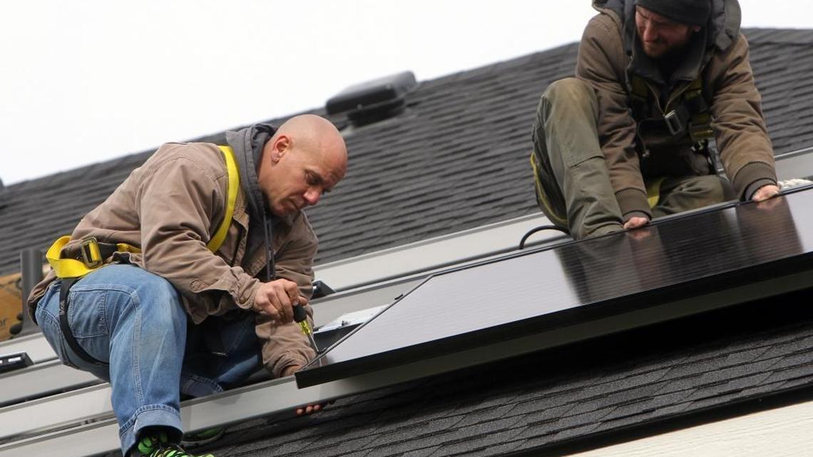 Ryan King, left, and Joziah Curry of EvenGreen Technology install solar panels on the roof of a home in the Harris Ranch subdivision.