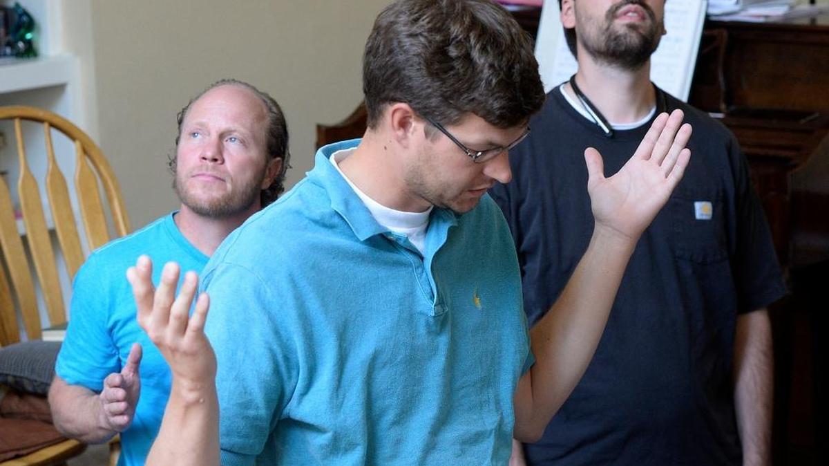 Members of Denver Snuffer’s Remnant movement meet in a Sandy, Utah home Aug. 13 to sing hymns and take sacrament. Scott Fisher, center, blesses the sacrament while Ken Jensen, left, and Taylor Child, right, look upward. Many in the movement believe that the LDS Church has strayed from its origins from Joseph Smith and reject the present structure and authority and believe anyone can receive revelations.