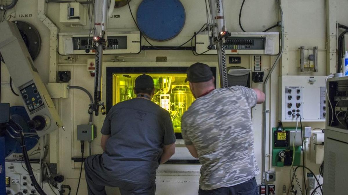 From left, Freddy Rodriguez and Brian Simmons, process nuclear operators at the INL, use master-slave manipulators to work with radioative material on the other side of the glass.