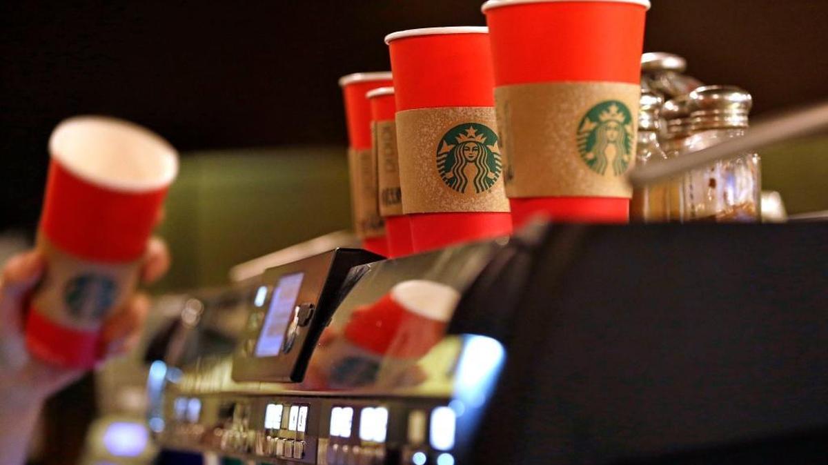 A barista reaches for a red paper cup as more, with cardboard liners already attached, line the top of an espresso machine at a Seattle Starbucks coffee shop Tuesday. It's as red as Santa's suit, a poinsettia blossom or a loud Christmas sweater. Yet Starbucks' minimalist new holiday coffee cup has set off complaints that the chain is ‘making war’ on Christmas. (AP)