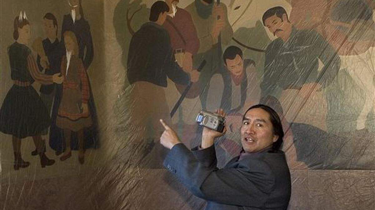 FILE - In this Jan. 17, 2007, file photo, Shoshone-Bannock Tribes Vice Chairman Lee Juan Tyler talks with others from his group while shooting some video of murals depicting the lynching of an Indian during a tour of the old Ada County Courthouse in Boise, Idaho. State officials are hosting a public hearing to determine if two historic murals should remain hidden from the public view. The murals include scenes of white settlers preparing to hang Native Americans. The paintings have caused controversy in the past, but now Idaho’s Historical Society is objecting to covering up the murals, calling them a part of the state’s history that the public can learn from.