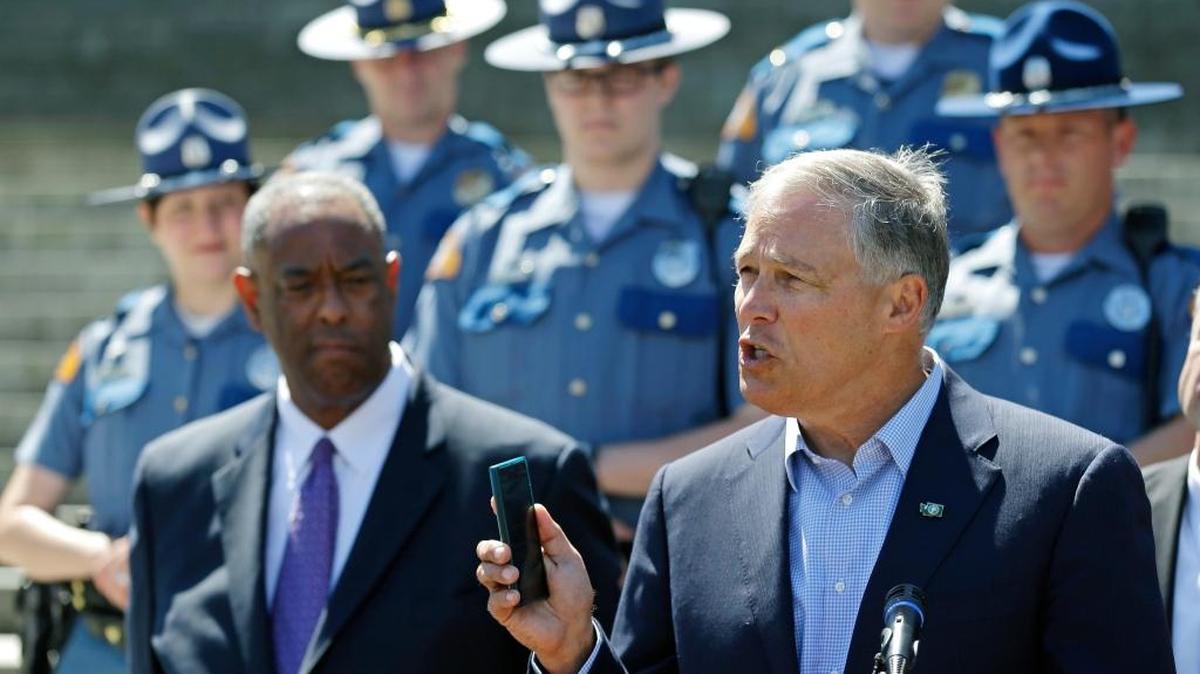During a speech in July, Washington Gov. Jay Inslee highlights the state’s new law prohibiting the use of nearly all phones and mobile devices while driving. At left is John Batiste, chief of the Washington State Patrol.