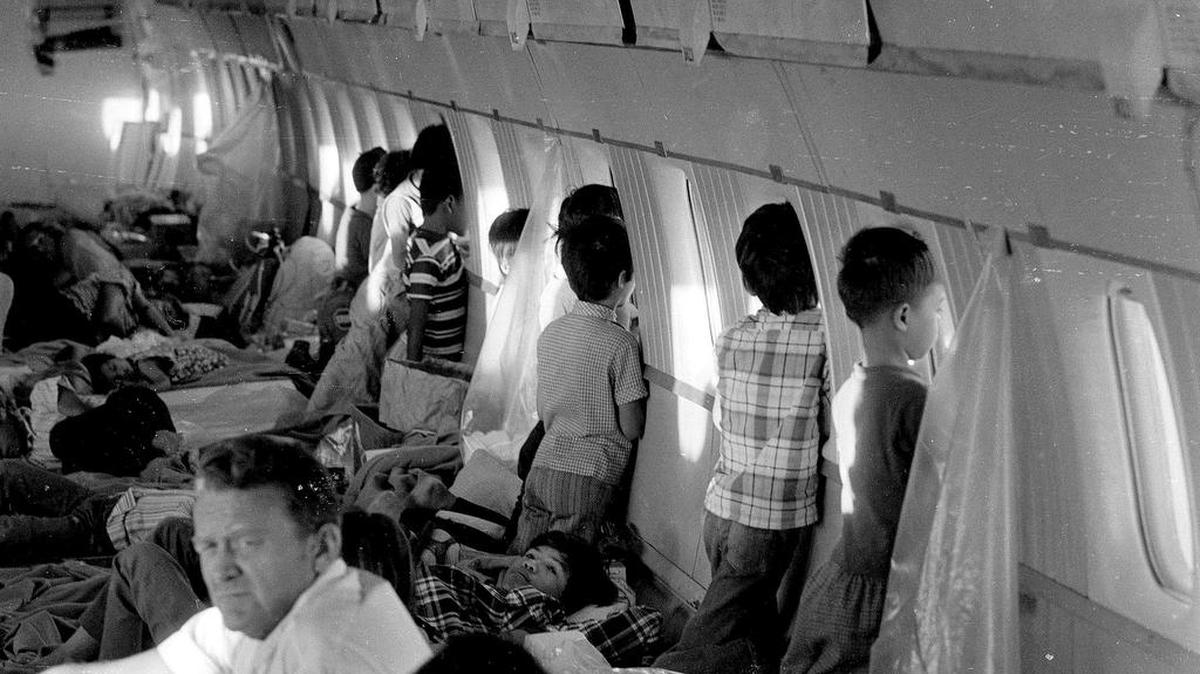 Refugee orphans from Vietnam aboard the first “Operation Babylift” flight at the end of the Vietnam War look through the windows of World Airways DC-8 jet as it flies them to the United States.