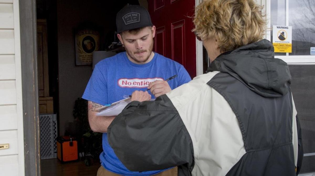 Trevor Buffi, Nampa, signs a petition for a Medicaid expansion initiative after meeting volunteer Laurie Durocher at the door in April.