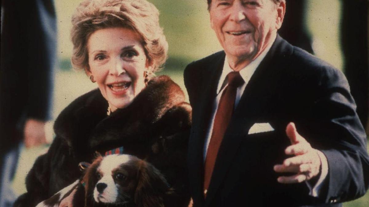 Then-President Ronald Reagan and Nancy Reagan, holding their dog, Rex, walk on the White House lawn in December 1986.