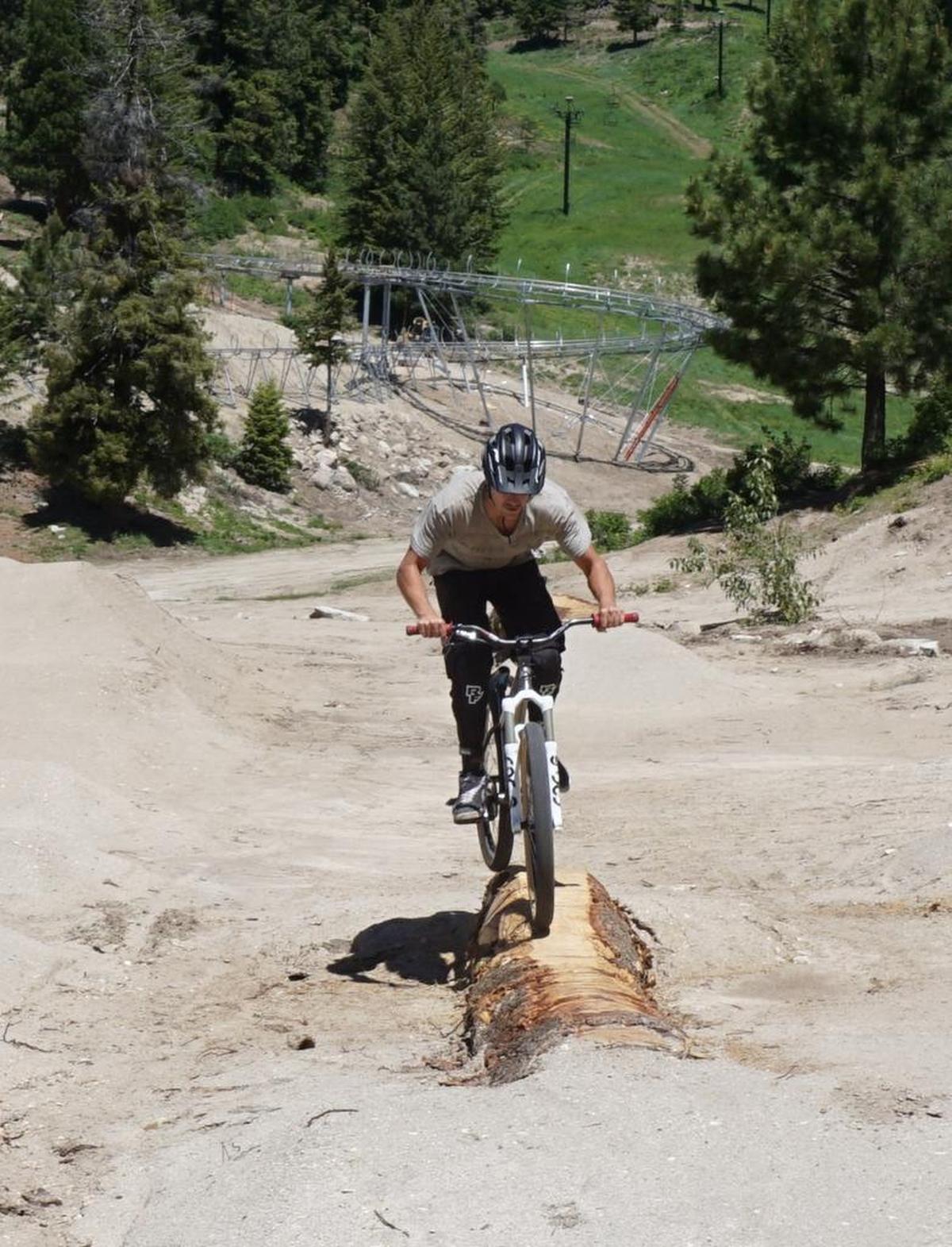 Austin Smith rides across a log in the bike park’s technical riding area — with the mountain coaster track behind him.