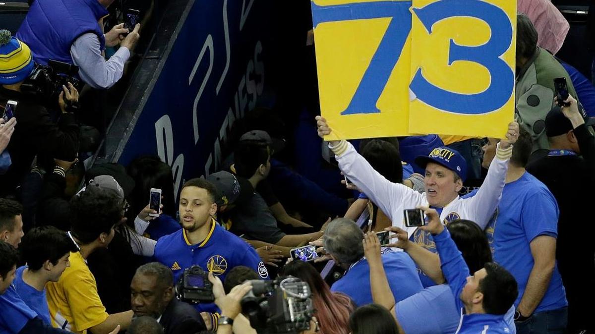 A Golden State Warriors fan holds up a 73 sign as Warriors guard Stephen Curry, bottom left, runs out of the tunnel before the Warriors and Memphis game Wednesday, April 13, 2016.